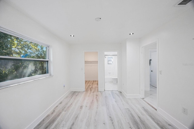 unfurnished bedroom with visible vents, light wood-style flooring, a walk in closet, and baseboards