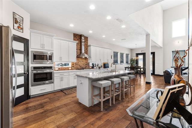 kitchen featuring visible vents, wall chimney range hood, appliances with stainless steel finishes, white cabinetry, and dark wood-style flooring