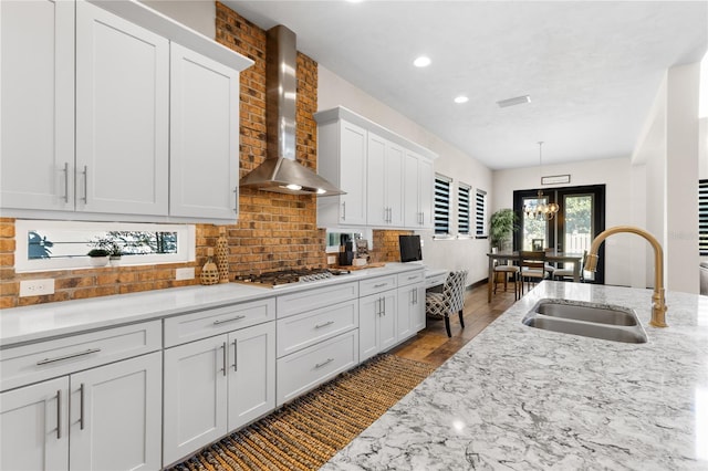 kitchen with decorative backsplash, stainless steel gas stovetop, white cabinetry, wall chimney exhaust hood, and a sink