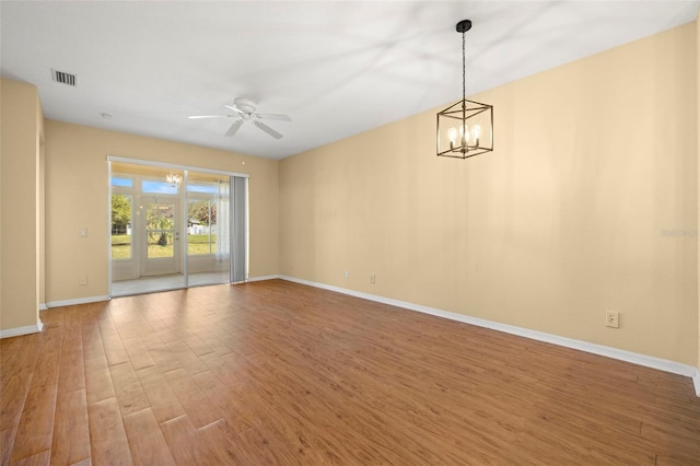 spare room featuring visible vents, ceiling fan with notable chandelier, baseboards, and wood finished floors