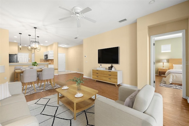 living area with visible vents, light wood-style flooring, ceiling fan with notable chandelier, and baseboards