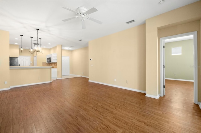 unfurnished living room with ceiling fan with notable chandelier, wood finished floors, visible vents, and baseboards