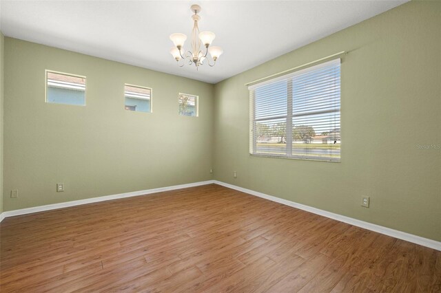 empty room with a chandelier, baseboards, and wood finished floors