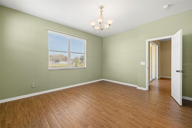 unfurnished room featuring baseboards, an inviting chandelier, and wood finished floors