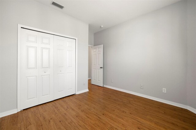 unfurnished bedroom featuring wood finished floors, visible vents, a closet, and baseboards