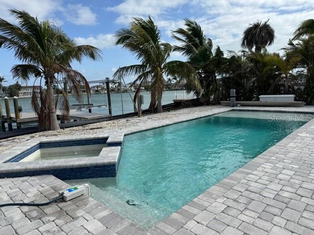 view of pool with a patio area, a water view, and a pool with connected hot tub