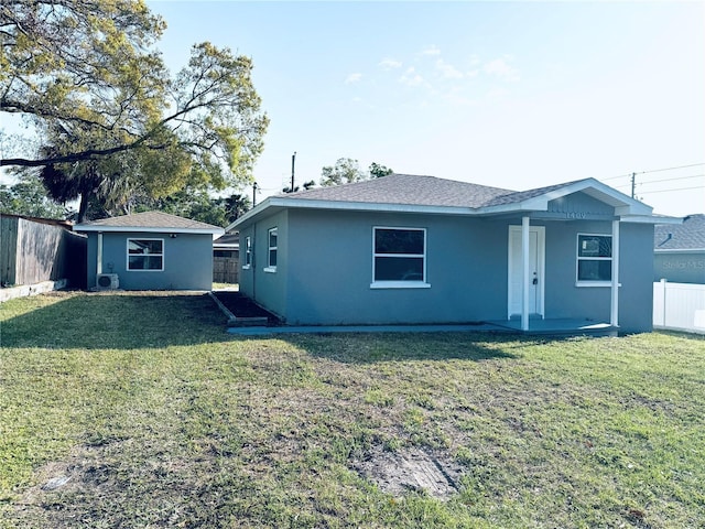 rear view of house with stucco siding, an outdoor structure, a yard, and fence