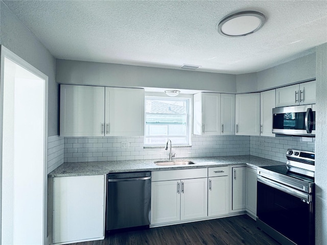 kitchen with dark wood-type flooring, a sink, stainless steel appliances, white cabinets, and decorative backsplash