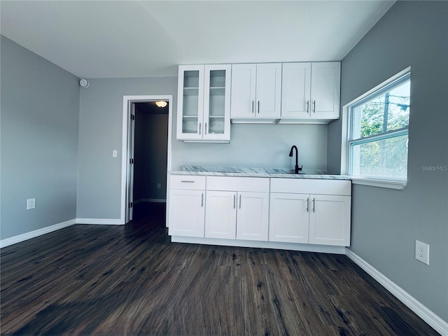 kitchen with dark wood-type flooring, glass insert cabinets, baseboards, white cabinetry, and a sink