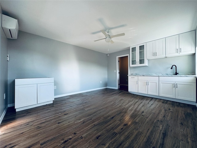 interior space featuring dark wood-type flooring, baseboards, ceiling fan, an AC wall unit, and white cabinets