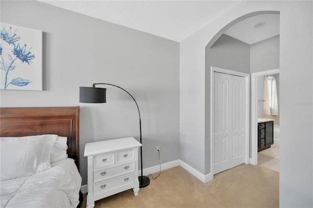 bedroom featuring a closet, light colored carpet, arched walkways, and baseboards