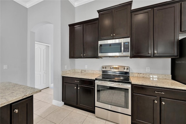 kitchen featuring dark brown cabinetry, ornamental molding, light tile patterned floors, arched walkways, and stainless steel appliances