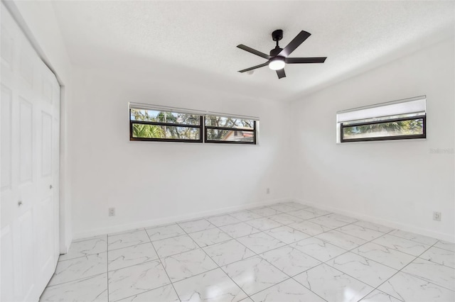 spare room with a ceiling fan, baseboards, marble finish floor, and a textured ceiling