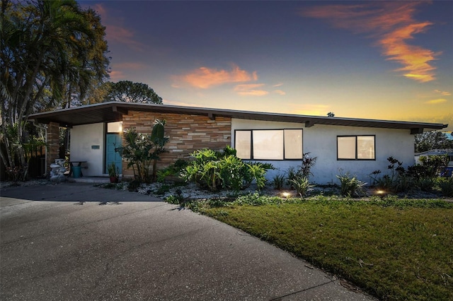 view of front of home with stucco siding, stone siding, a lawn, and concrete driveway