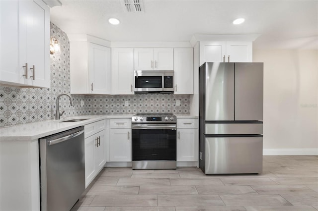 kitchen with a sink, decorative backsplash, light countertops, stainless steel appliances, and white cabinetry