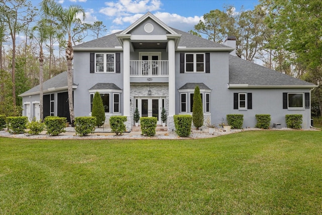 view of front of property with a front yard, a balcony, french doors, and a chimney