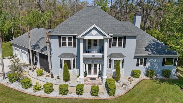 neoclassical home with a balcony, french doors, a chimney, and stucco siding