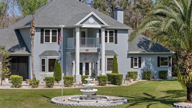 view of front facade with stucco siding, french doors, a front yard, a shingled roof, and a balcony