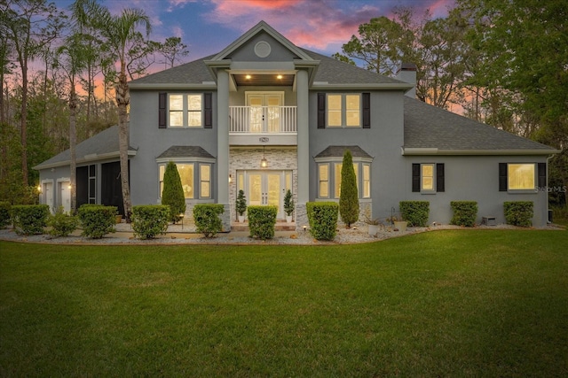 view of front facade featuring stucco siding, french doors, a front lawn, and a balcony