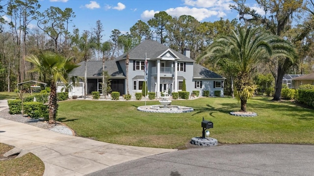 view of front facade with a front yard, a balcony, and a chimney