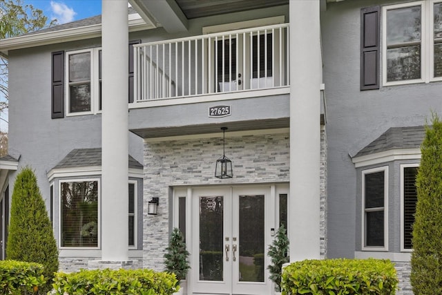 view of exterior entry with a balcony, french doors, stone siding, and stucco siding