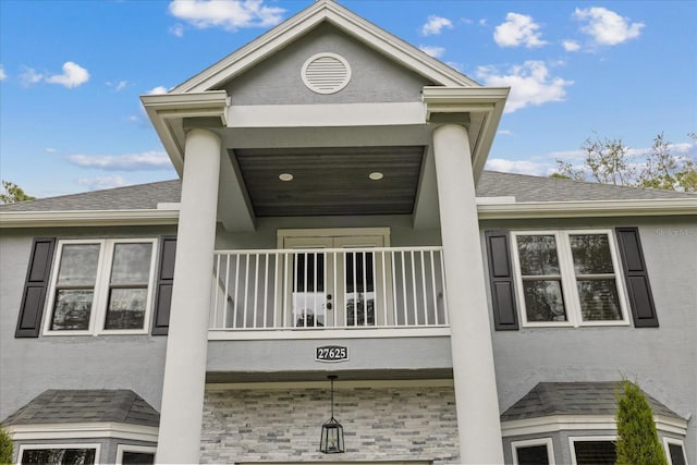 exterior space featuring stucco siding, a shingled roof, and a balcony