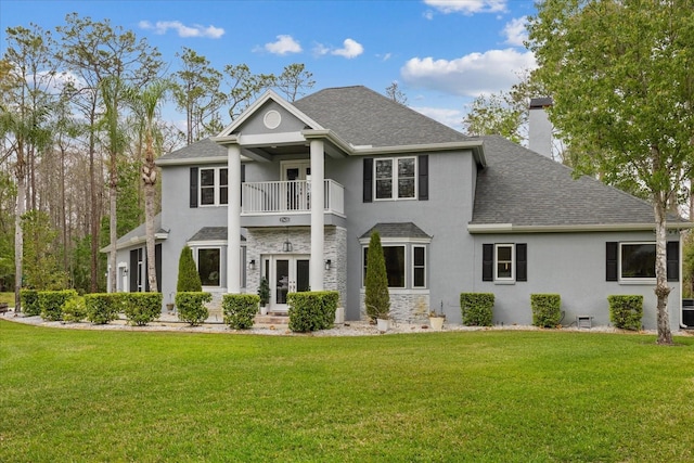 greek revival house with stucco siding, french doors, a front yard, a balcony, and a chimney