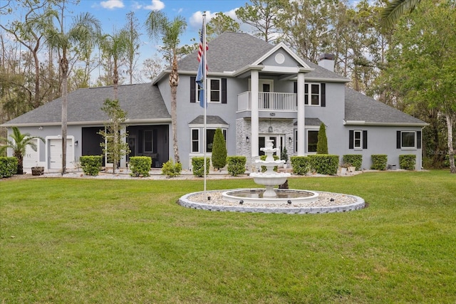 rear view of property featuring a balcony, a yard, a shingled roof, stucco siding, and a chimney