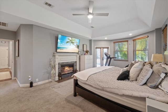 bedroom featuring visible vents, baseboards, a fireplace with flush hearth, light colored carpet, and a tray ceiling