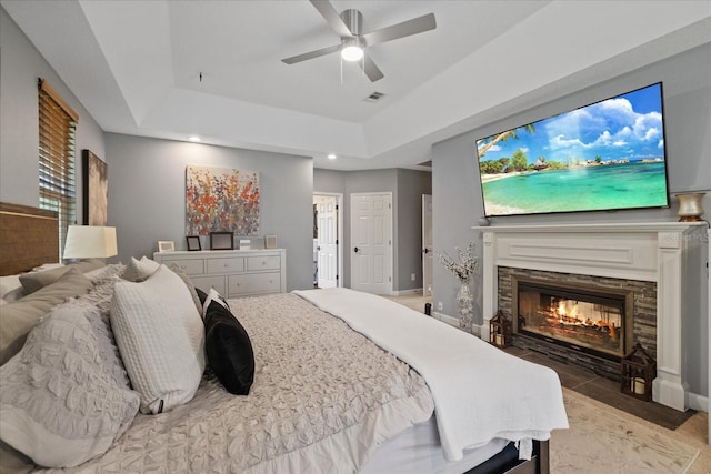 bedroom featuring a fireplace with flush hearth, a tray ceiling, recessed lighting, baseboards, and ceiling fan