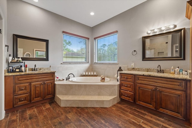 full bath with a sink, two vanities, wood finished floors, and a bath