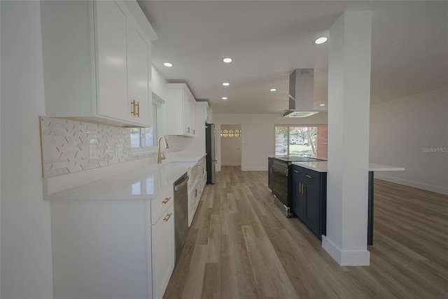 kitchen featuring a sink, white cabinetry, appliances with stainless steel finishes, wall chimney exhaust hood, and decorative backsplash