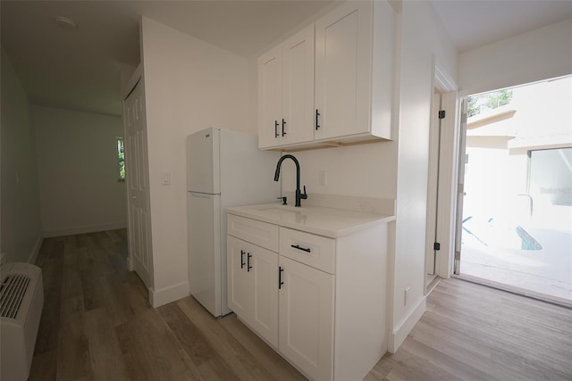 kitchen with light countertops, light wood-type flooring, freestanding refrigerator, white cabinets, and a sink