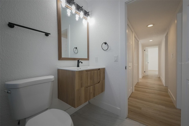 bathroom with vanity, toilet, a textured wall, and baseboards