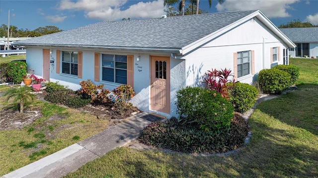 view of front of property with a front yard, roof with shingles, and stucco siding