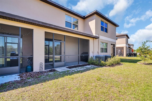 back of property with central AC unit, a lawn, a sunroom, and stucco siding