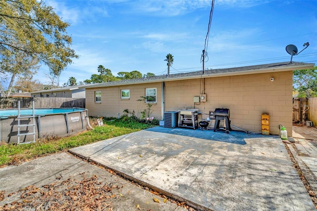 rear view of property with fence, cooling unit, concrete block siding, an outdoor pool, and a patio