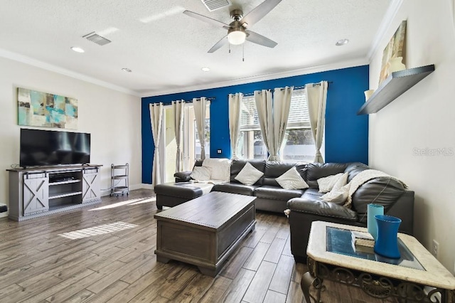 living room with ceiling fan, visible vents, wood finished floors, and ornamental molding