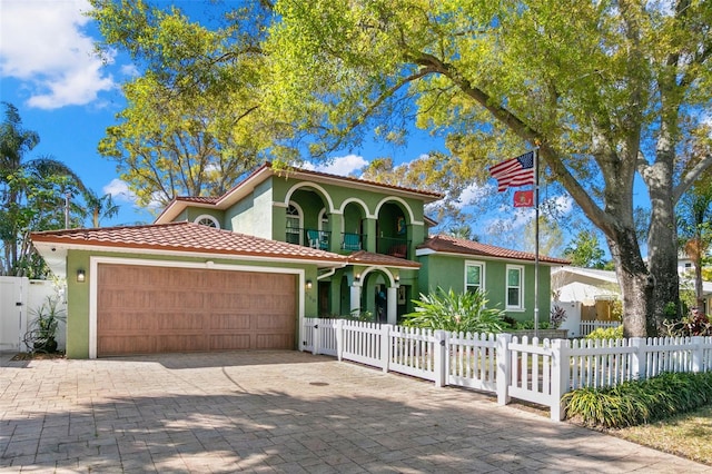 mediterranean / spanish-style home with a gate, stucco siding, a garage, a fenced front yard, and a tile roof