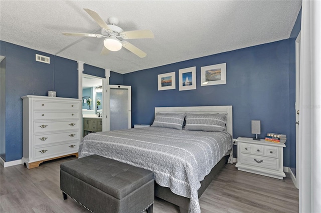 bedroom with baseboards, wood finished floors, visible vents, and a textured ceiling