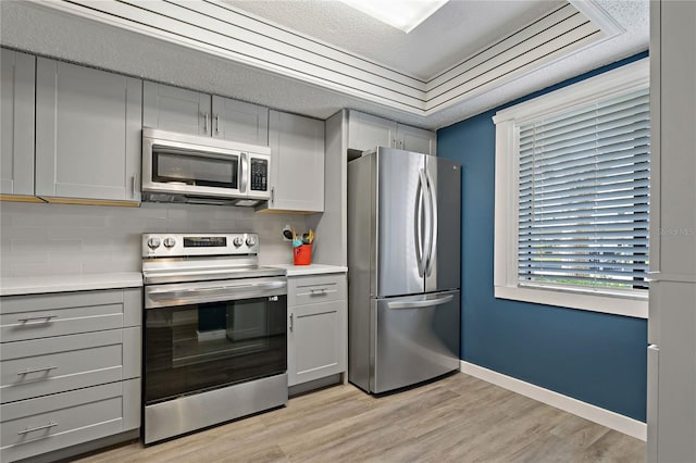 kitchen with gray cabinetry, baseboards, light countertops, light wood-style flooring, and stainless steel appliances