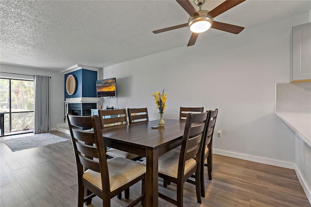 dining area featuring dark wood-type flooring, a textured ceiling, a fireplace, baseboards, and ceiling fan