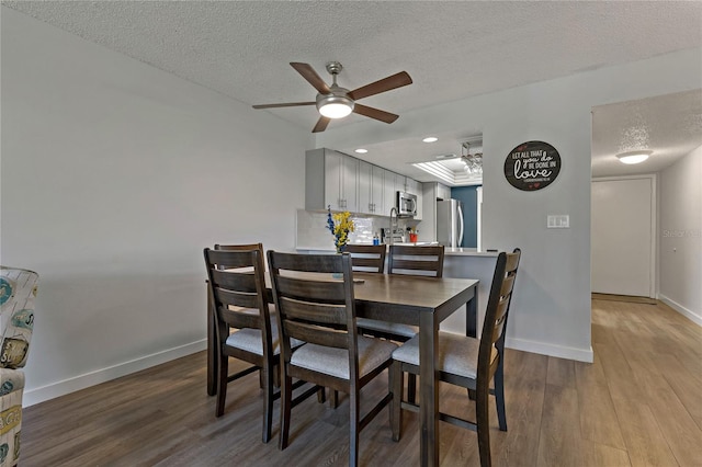 dining space with wood finished floors, a ceiling fan, baseboards, and a raised ceiling