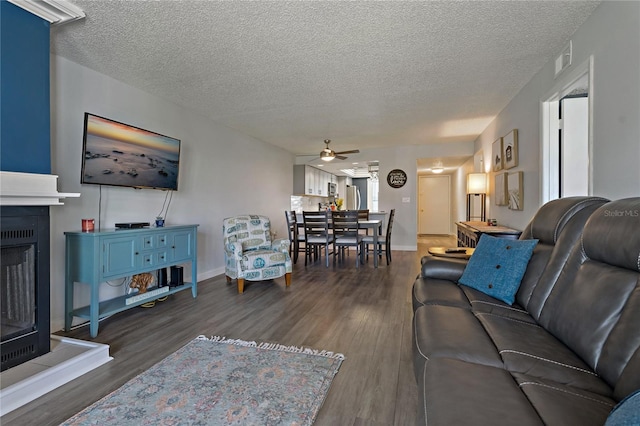 living area with a fireplace with raised hearth, a textured ceiling, a ceiling fan, and wood finished floors