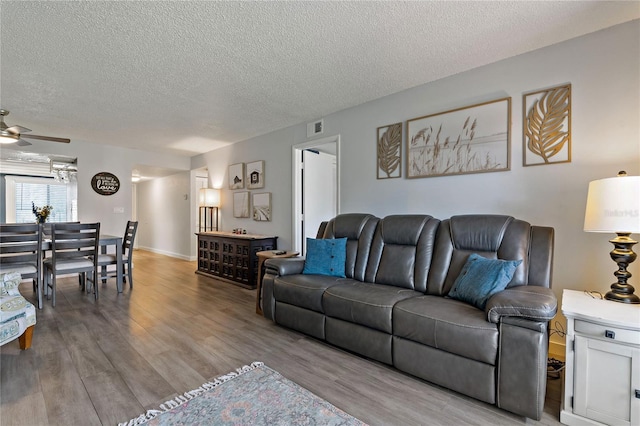 living room featuring a textured ceiling, a ceiling fan, visible vents, and light wood-type flooring