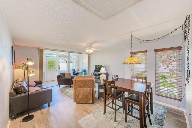 dining room with light wood-style flooring, a ceiling fan, baseboards, and a textured ceiling