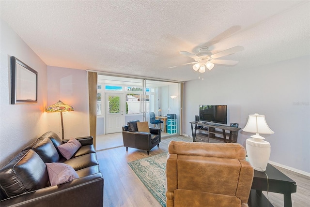 living room featuring baseboards, a textured ceiling, ceiling fan, and light wood finished floors