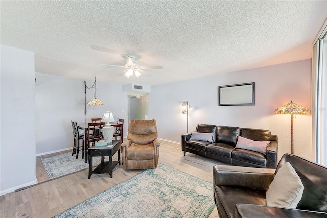 living area with visible vents, a ceiling fan, light wood-type flooring, and a textured ceiling