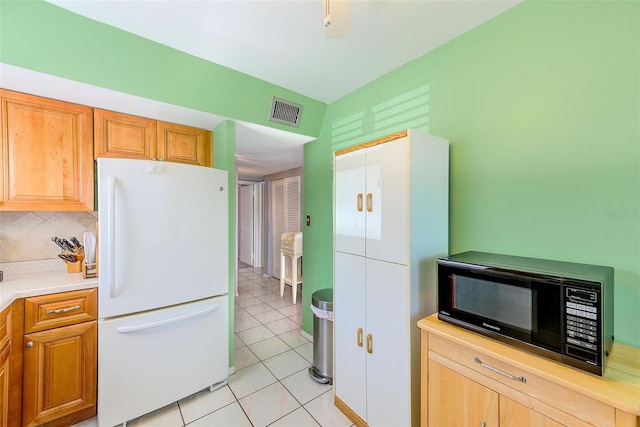 kitchen with light tile patterned floors, visible vents, freestanding refrigerator, decorative backsplash, and black microwave