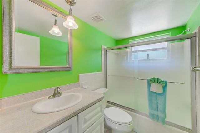 full bathroom with vanity, toilet, visible vents, and shower / bath combination with glass door